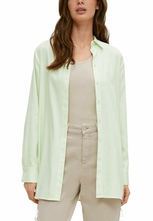 Chemise boutonnée vert clair à rayures verticales, manches longues, coupe décontractée, associée à un débardeur beige côtelé et un pantalon beige clair.