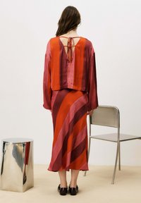 Ensemble deux pièces rayé rouge et rose comprenant un top court dos nu et une longue jupe à motifs diagonaux. Texture lisse.