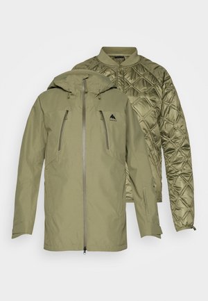 Veste d'extérieur verte avec une doublure matelassée amovible, poches zippées et capuche ajustable. Coque extérieure texturée et doublure lisse.