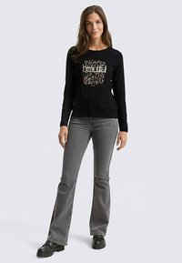 Maglietta nera a maniche lunghe con grafica "beautiful" in bianco e accenti dorati, abbinata a jeans grigi a zampa e scarpe platform nere.