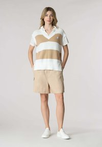 Polo a righe bianche e beige in maglia con scollo a V e maniche corte, abbinato a pantaloni cargo beige e sneakers bianche.
