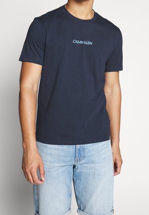Marineblaues Baumwoll-T-Shirt mit kurzen Ärmeln, rundem Ausschnitt und "CALVIN KLEIN"-Logo in Hellblau quer über der Brust platziert.
