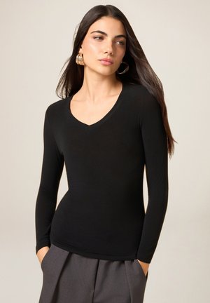 Czarna bluzka z długim rękawem i dekoltem w serek, wykonana z gładkiego materiału, o dopasowanym kroju i subtelnym połysku. Połączona z wysokim stanem szarymi spodniami.