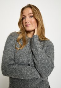 Sivý pletený kardigán s jemnou textúrou, s gombíkmi vpredu, širokými rukávmi a mierne oversize strihom.