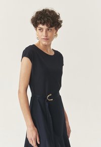 Navy blue dress with short sleeves, round neckline, and a belted waist featuring a gold circular buckle. Smooth fabric and A-line shape.
