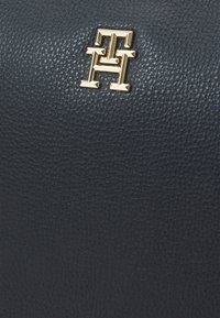 Borsa in pelle testurizzata blu navy con un logo dorato ben in evidenza. La superficie presenta una finitura a grana fine con dettagli di pattern distintivi.