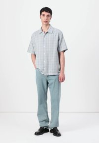 Kurzarm-Hemd in Hellblau mit vertikalen Streifen, kombiniert mit hellblauen Jeans und schwarzen Schuhen. Einfaches, lässiges Design.