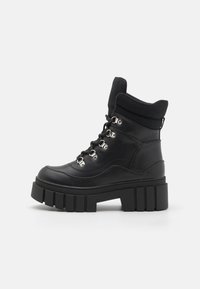 Bottines noires à plateforme épaisse, avec une tige en cuir lisse, des lacets avec œillets métalliques et un col rembourré.