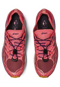 Red athletic shoes with a textured mesh upper, featuring a lacing system, logo detail, and a patterned design. Outsole has rubber accents.
