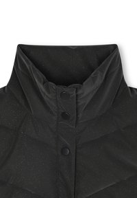 Primo piano di un colletto di una giacca imbottita nera con colletto alto, caratterizzato da due bottoni rotondi e una texture leggermente lucida con sottili granuli.