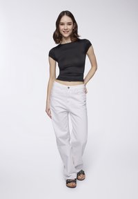 Top nero aderente a maniche corte abbinato a pantaloni bianchi a vita alta e a gamba larga. Calzature con un design a piattaforma nera con borchie.