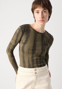 Olive green ribbed long-sleeve top featuring a round neckline and subtle tie-dye pattern, paired with a light-colored skirt with detailed seams.