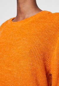 Oranger Strickpullover mit rundem Halsausschnitt. Texturiert, lockere Passform und sichtbare Nähte. Weiches, warmes Material.