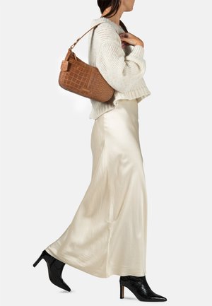 Sac à bandoulière en cuir marron embossé crocodile, pull en tricot crème, jupe longue blanche soyeuse, et bottines noires à talons pointus.