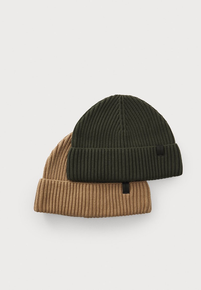 Two ribbed knit beanies: one olive green on top, one light tan underneath. Both have a folded brim and a small black tag.