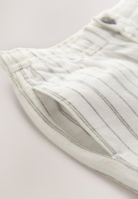 Shorts en lin couleur crème clair avec fines rayures grises, dotés d'une taille élastique et de poches latérales. Texture douce avec une coupe décontractée.