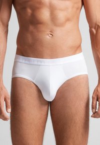 Hvide mænds briefs lavet af glat stof, med en strækbar talje med præget logo. Designet inkluderer en frontlomme og ingen synlige sømme.