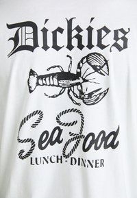 Hvit bomulls T-skjorte med et svart hummerdesign og fet tekst som sier "Dickies Seafood Lunch-Dinner" i varierte skrifttyper.