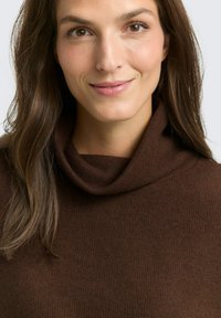 Pull en col roulé marron à côtes avec une texture douce, doté d'un décolleté cowl décontracté. Conception lisse et ajustée autour du col.