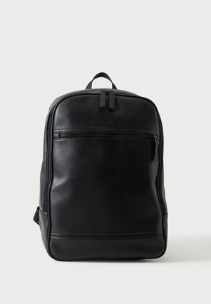 Sac à dos en cuir noir avec poche avant zippée, compartiment principal à double fermeture éclair et poignée de transport supérieure sur fond neutre.