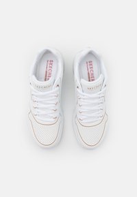 White Skechers sneakers with perforated upper, pink cushioned insole, and light tan accents. Laces and rounded toe design.