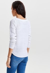 Maglione bianco lavorato a maglia con maniche lunghe e polsini a coste, caratterizzato da una scollatura arrotondata e una vestibilità leggermente ampia, abbinato a un paio di jeans blu.