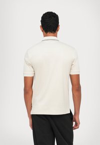 Crème kortemouwen polo shirt met een kraag, voorzien van een zwarte rand bij de hals, textuurstof en een zijsplit aan de zoom.