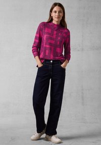 Fuchsia-gepatrooneerde sweater met geometrische vormen, gecombineerd met donkerblauwe straight-leg jeans en beige sneakers. Textuurstof, losse pasvorm.