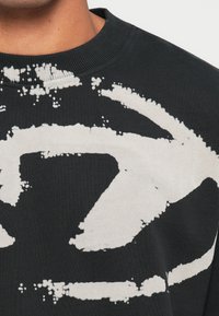 Sweatshirt preta com um grande padrão abstrato branco. O material é macio, com um decote redondo canelado e uma textura ligeira.