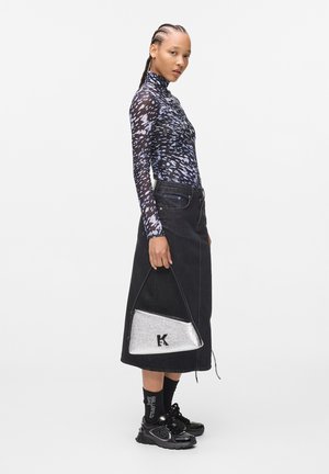 Gonna di denim nera con orlo asimmetrico, top aderente a maniche lunghe con motivo blu e bianco, e una borsa a spalla argentata con logo.