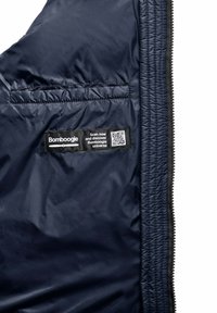 Marineblauwe pufferjack met een gladde, glanzende textuur. Voorzien van een rits aan de voorkant, een zijzak en een label met merknaam en een QR-code.