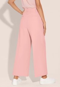 Lichte roze wijde broek met hoge taille, soepele textuur, achterzakken en een nette afwerking, gecombineerd met witte sneakers.