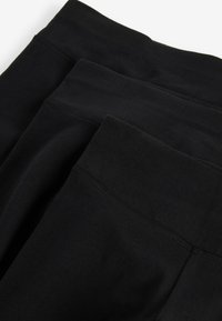 Schwarze Leggings aus einem glatten Stoff mit einem breiten Bund und ohne sichtbare Nähte. Das Material wirkt dehnbar und leicht.