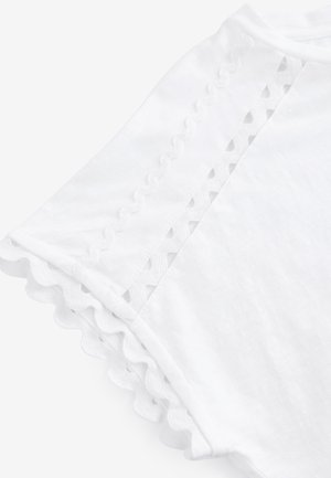 Hvid kortærmet skjorte med bølget kant og dekorativt blondetrim langs ærmet og skuldersømmen.