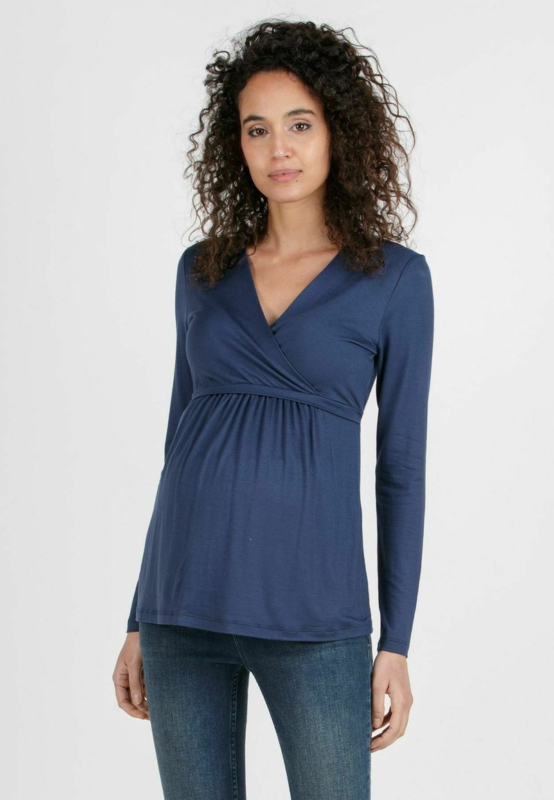 Navy-blaues langärmliges Stilloberteil mit Wickeldesign, V-Ausschnitt und Raffung unter der Brust. Glattes Material mit weicher Textur.