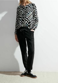 Camicia a maniche lunghe con motivo geometrico in bianco e nero abbinata a pantaloni neri con coulisse. Sneakers nere con lacci bianchi.