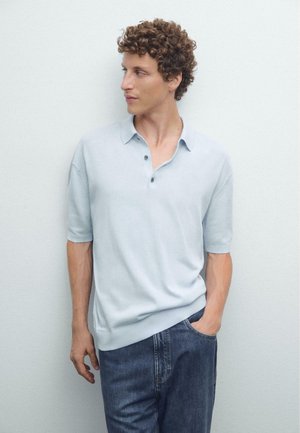 Hellblaues kurzärmeliges Poloshirt mit Kragen und drei Knopfverschluss, kombiniert mit dunklen Jeans. Glatte Maschenstruktur.