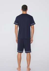 Ensemble de loungewear en tricot marine avec des bordures blanches, comprenant un t-shirt à manches courtes et un short au-dessus du genou, conçu pour le confort et la liberté de mouvement.