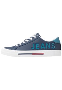 Navy sneaker with white laces and rubber sole. Features "JEANS" in turquoise. Accented with red and blue stripes on the white sole.