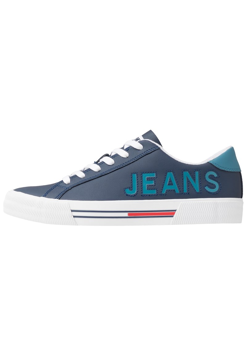 Navy sneaker with white laces and rubber sole. Features "JEANS" in turquoise. Accented with red and blue stripes on the white sole.