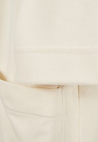 Light beige sweatshirt with textured hem, soft fabric, and a visible side pocket. The design features a casual, relaxed fit.