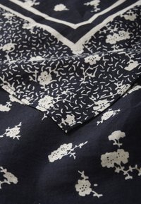 Tejido azul marino con un patrón floral en blanco, con una superficie texturada y bordes distintivos, que muestra una combinación de diseños intrincados.