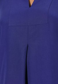 Blusa con scollatura a V in tessuto blu reale unito, caratterizzata da una piega frontale e un design leggermente strutturato, texture liscia e cuciture curate.