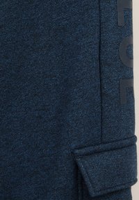 Tissu en tricot bleu foncé à motifs, avec un revers replié et un texte vertical partiel imprimé en noir sur le côté.