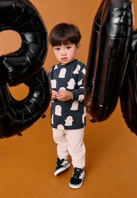Long-sleeve shirt with ghost pattern in dark blue, paired with white pants and black/white shoes, against a brown background with black balloons.
