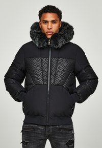 Giacca a vento nera con un ampio colletto in pelliccia sintetica, motivo a rombi sui pannelli superiori e chiusura con zip. Presenta polsini e orlo a coste.