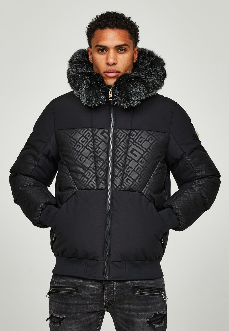 Giacca a vento nera con un ampio colletto in pelliccia sintetica, motivo a rombi sui pannelli superiori e chiusura con zip. Presenta polsini e orlo a coste.