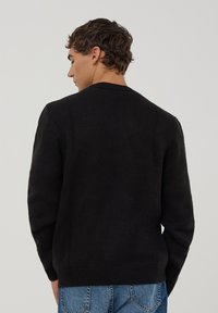 Czarny sweter dzianinowy z okrągłym dekoltem i prążkowanymi mankietami. Tekstura wydaje się gładka, a sweter jest zestawiony z niebieskimi dżinsami.