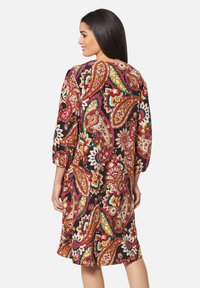 Schwarzes Kleid mit einem lebhaften Paisleymuster in Rot, Gelb und Grün; Dreiviertelärmel und lockere Passform.