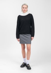 Zwarte trui met een lichte glans, losse pasvorm, brede halslijn; grijze rok met witte streepjes; zwarte instappers; witte enkelsokken.